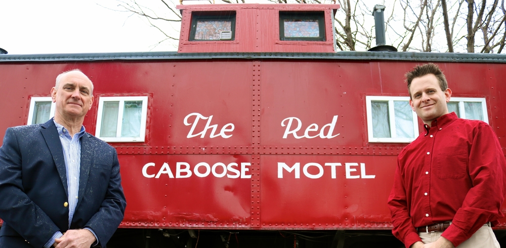 father and son owners standing in front of Red Caboose Motel sign